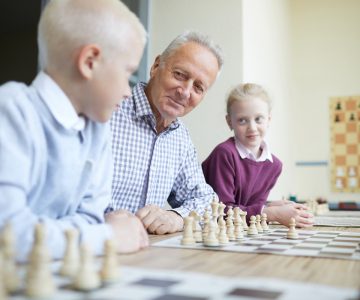 Smiling grandfather in checked shirt teaching his two curious grandkids how to play chess (zh translation)